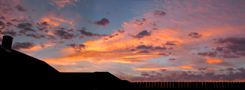 [Several photos stitched together expanding the view to the right across the fenced yard. There is little blue sky visible among the melon, lavender, and purple clouds.]